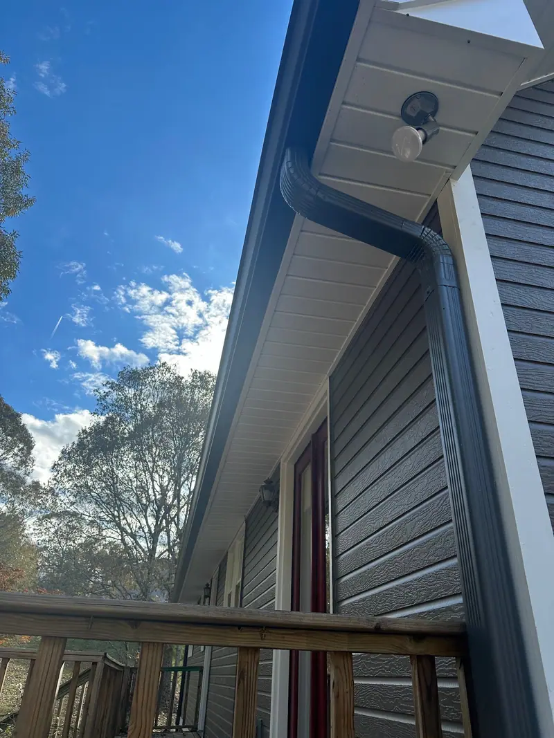 Dark gutter and downspout under a white soffit on gray lap siding, a Mosqueda Construction gutter job