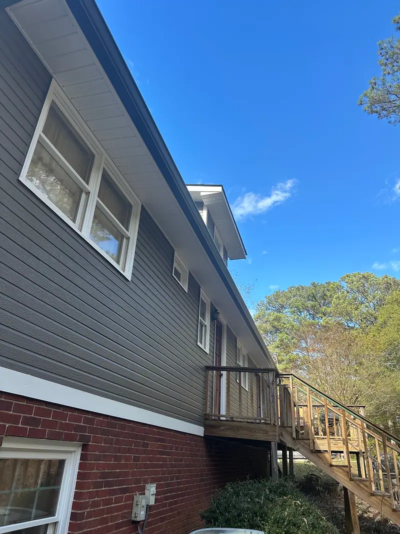 Dark gray lap siding over a brick foundation with new wood deck stairs, a Mosqueda Construction siding job